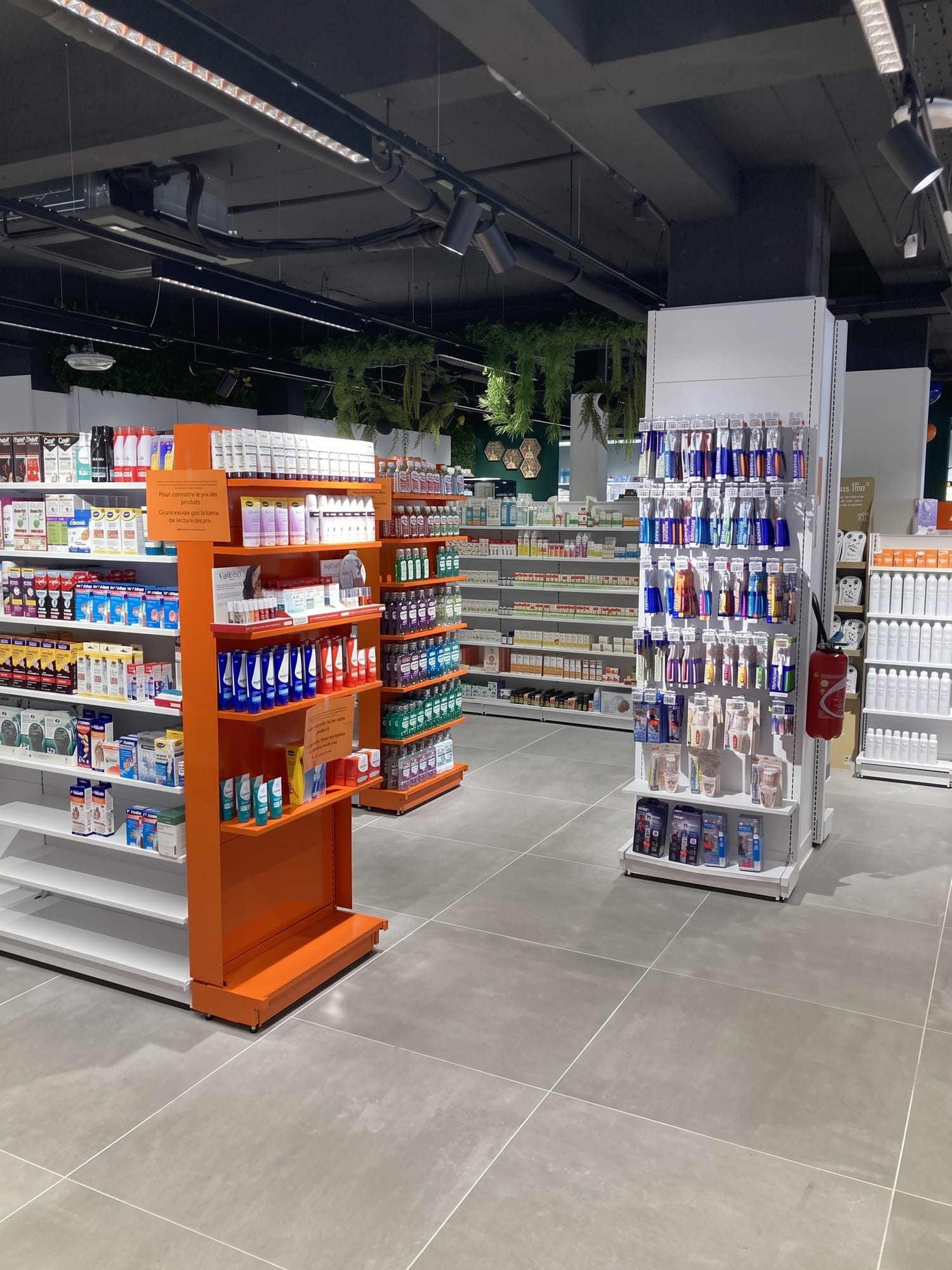 Espace de vente de la Pharmacie Errera, gondoles orange et végétation suspendue
